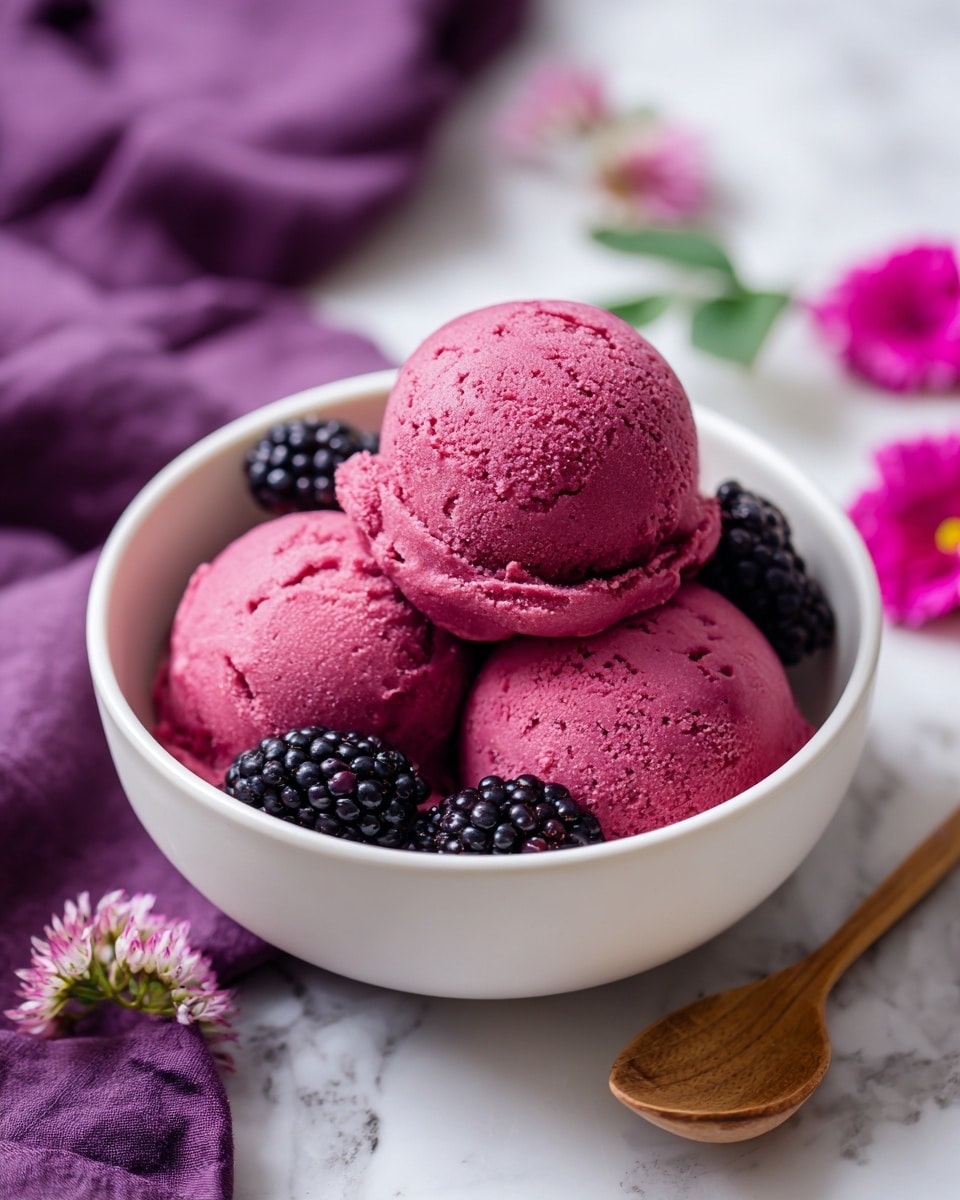 The image shows three deep pink ice cream scoops stacked inside a white bowl with blackberries placed around them inside the bowl. Around the bowl, more blackberries are scattered on a white marbled surface. The background has a bright purple fabric with small light purple flowers placed nearby. Two small wooden spoons are also lying on the white marbled surface in front of the bowl. photo taken with an iphone --ar 4:5 --v 7