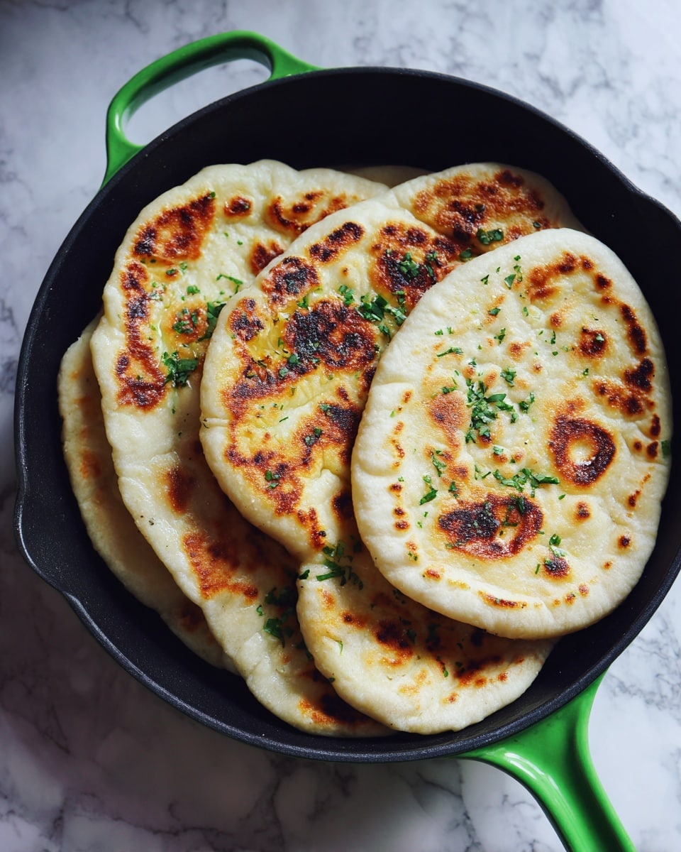 The image shows four golden brown flatbreads with uneven crispy spots, each folded in half and arranged closely inside a green cast iron pan. The flatbreads have light and dark toasted areas with a soft, slightly puffy texture. Small green herb leaves are sprinkled on top. The pan sits on a white marbled surface. photo taken with an iphone --ar 4:5 --v 7