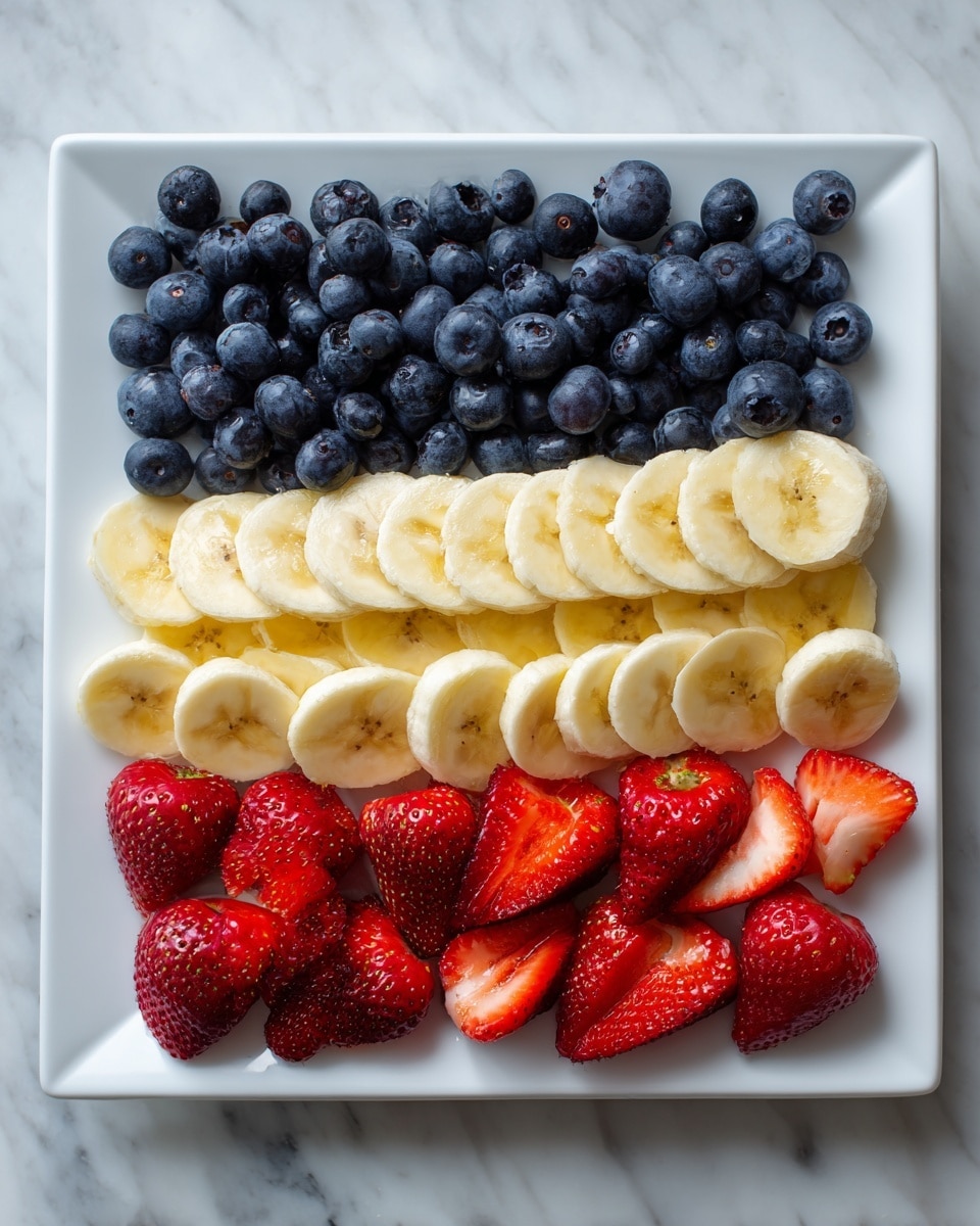 A white square plate shows an arrangement of fresh fruit layers forming an American flag pattern. The top left corner is a dense square of dark blue blueberries. To the right, there is a line of banana slices followed by a line of whole and halved strawberries mixed together, showing red color and green tops. Below the blueberries, two full rows of banana slices create a light yellow stripe. The next two rows beneath are made of whole and halved strawberries, bright red with green leaves. The plate is on a white marbled surface. photo taken with an iphone --ar 4:5 --v 7