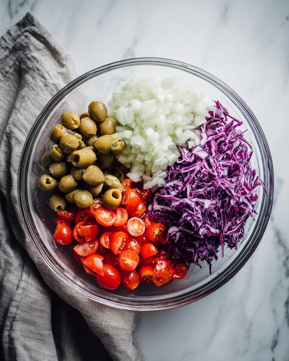 A clear glass bowl on a white marbled surface holds four separate layers of ingredients, each in its own section. The top right section has small white chopped onions with a rough texture. Below the onions, to the right bottom, is a pile of thinly shredded purple cabbage that looks fresh and crisp. The bottom left section contains small red cherry tomatoes, some cut in half, showing their juicy inside. The top left section has green olives stuffed with red pimentos, smooth and round. The bowl is next to a soft gray cloth. Photo taken with an iphone --ar 4:5 --v 7