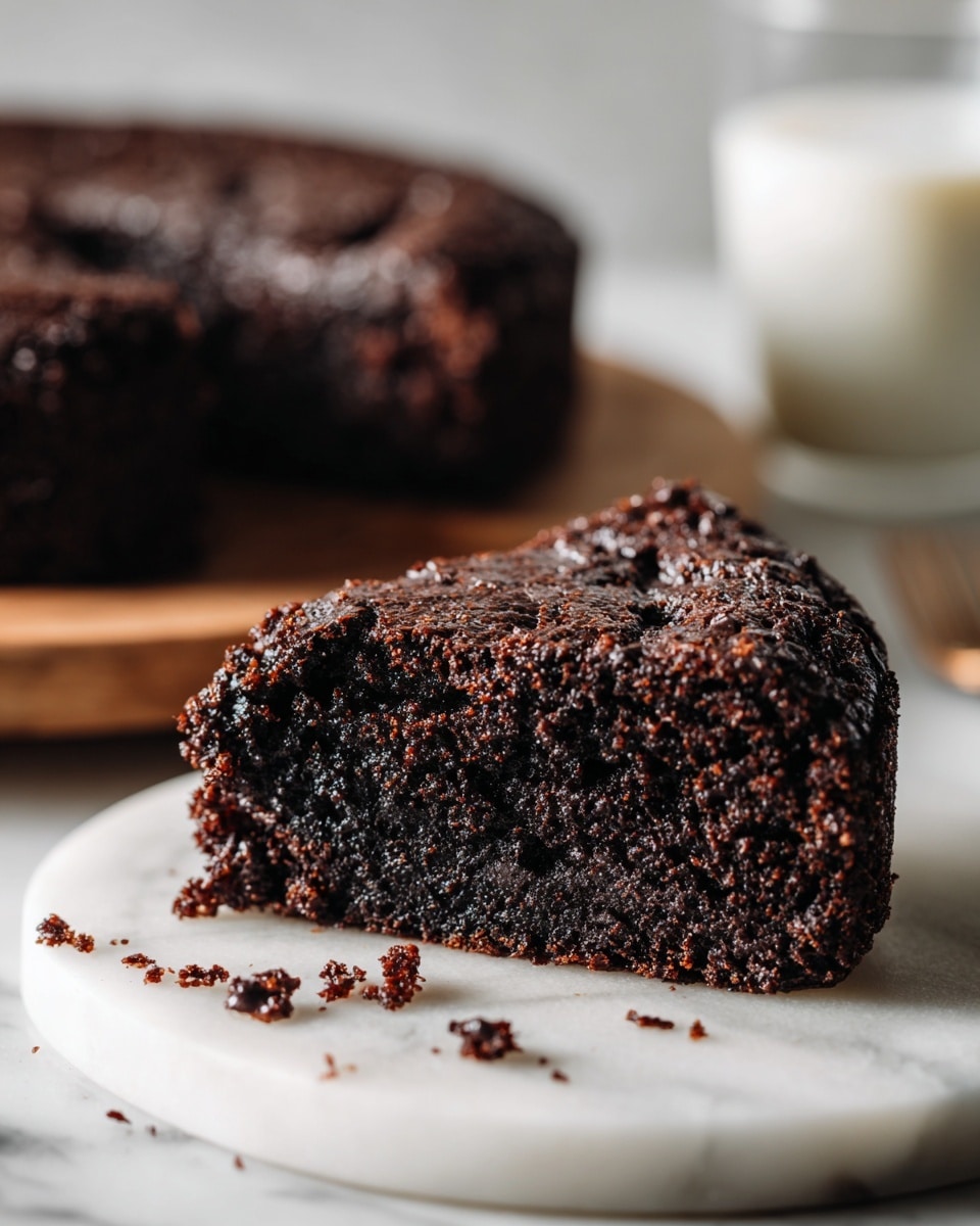 A close-up of a piece of dark brown chocolate cake with a rough, crumbly texture on a white marbled surface. The cake piece shows moistness inside and some chocolate chips or chunks embedded in it. Crumbs are scattered around the piece. In the background, the rest of the chocolate cake is partially visible on a wooden board. There is also a glass of white liquid, probably milk, next to the cake. Photo taken with an iphone --ar 4:5 --v 7