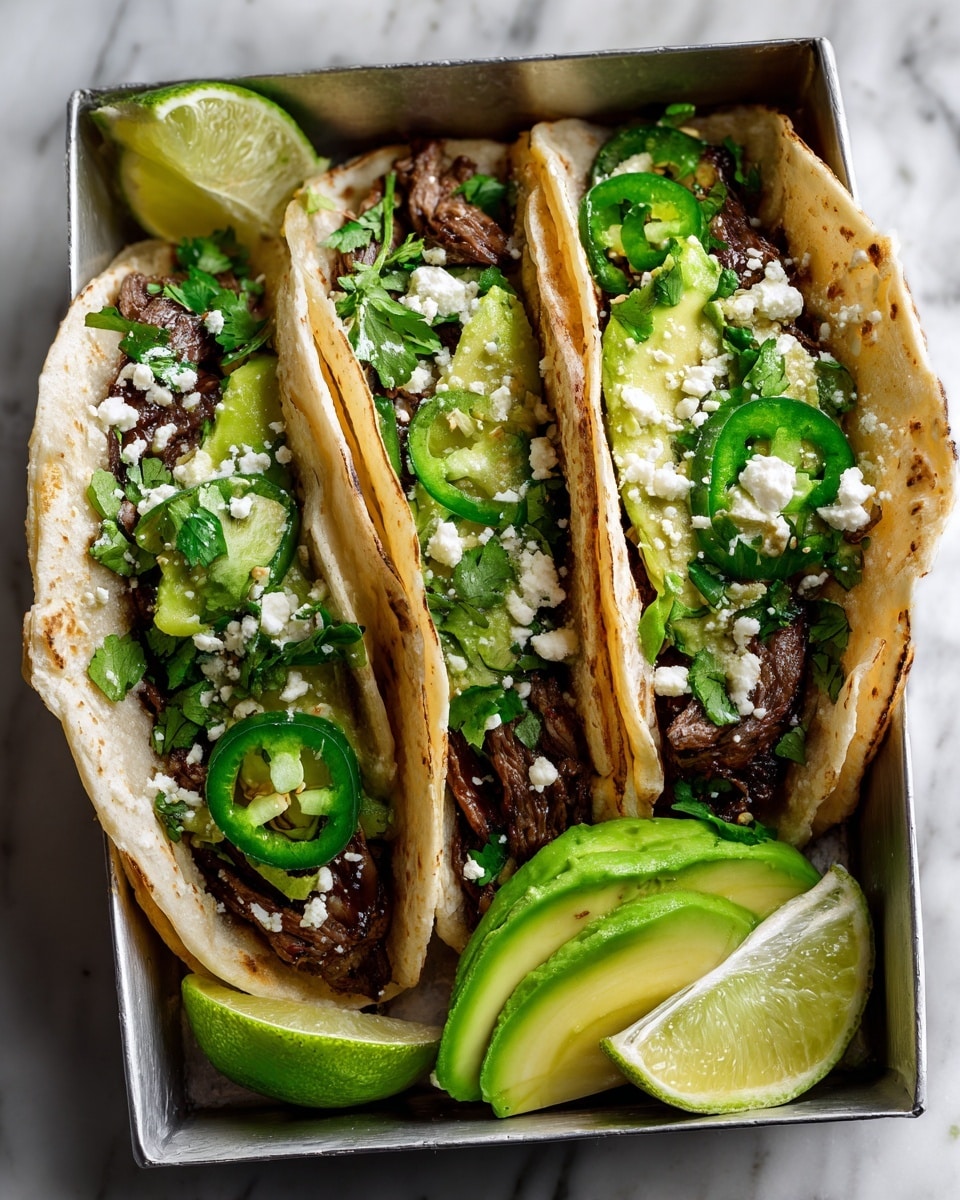 Three soft corn tortillas hold layers of grilled steak slices that are dark brown with a charred texture, topped with small green avocado cubes, bright green cilantro leaves, and slices of green jalapeño peppers. White crumbled cheese is sprinkled over the toppings. The tacos rest in a silver taco holder placed on a white marbled surface, with lime wedges near the top right and a half avocado seen at the lower left. The overall colors are warm beige, rich brown, and fresh greens, giving a fresh and appetizing look. photo taken with an iphone --ar 4:5 --v 7