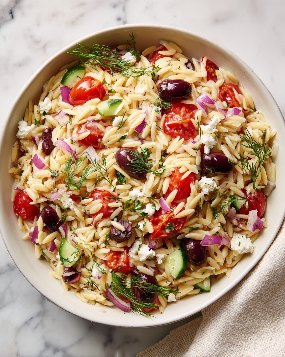 A white bowl filled with a fresh orzo salad containing small white pasta pieces mixed with bright red halved cherry tomatoes, chopped green cucumber slices, small black olives, finely chopped purple onion, and small white cubes of cheese scattered throughout. The salad is sprinkled with green dill leaves, all sitting on a white marbled surface. Photo taken with an iphone --ar 4:5 --v 7