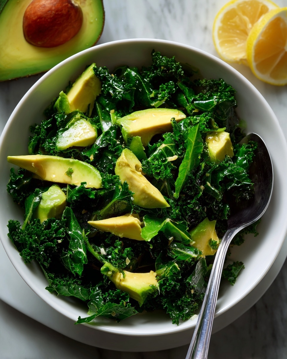 A white bowl filled with chopped curly kale as the base layer, dark green with a rough texture, mixed with chunks of bright yellow-green avocado pieces scattered on top. There is a light dressing giving a slight shine to the kale and avocado, sprinkled with tiny bits of black pepper and lemon zest. A silver fork is placed inside the bowl on the right side. The bowl sits on a white marbled surface with half an avocado and a lemon wedge placed nearby. Photo taken with an iphone --ar 4:5 --v 7