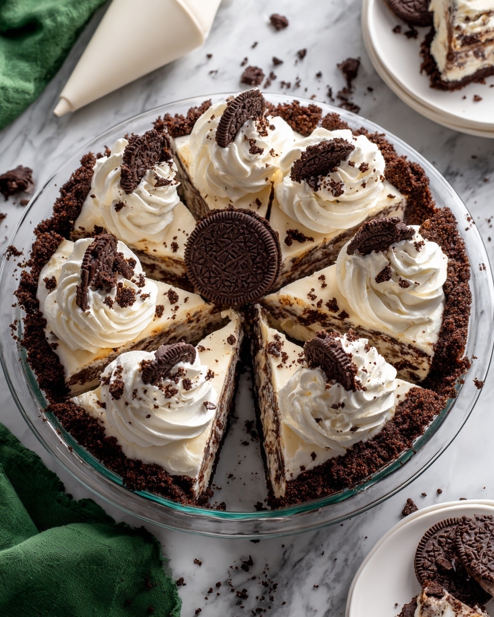 This image shows an Oreo cream pie in a clear glass pie dish with a dark chocolate crumb crust forming a thick outer edge. Inside the crust is a creamy white layer with crushed Oreo bits throughout, divided into eight slices. On top of each slice is a swirl of white whipped cream, and in the center of the pie sits a whole Oreo cookie. The pie is on a white marbled surface with some crumbs scattered around. A white piping bag with a metal tip lies nearby, along with a green cloth and some Oreo cookies on the side. Photo taken with an iphone --ar 4:5 --v 7