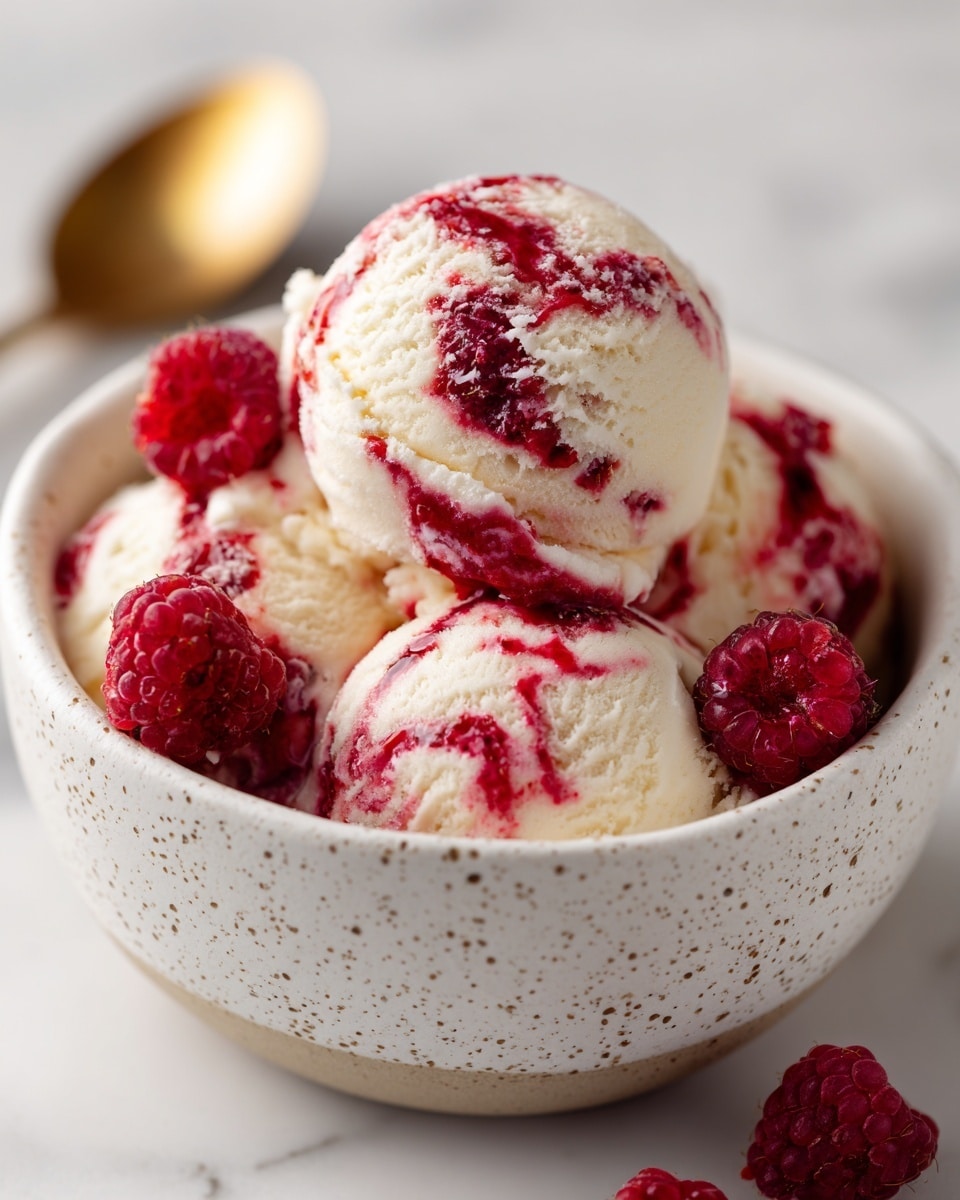The image shows a white speckled bowl filled with three large scoops of cream-colored ice cream with bright red swirls mixed throughout. Around the ice cream, several fresh raspberries are placed on the sides inside the bowl, showing their red color and bumpy texture. The bowl sits on a white marbled surface with subtle gray veins, and a gold spoon is blurred in the background. Additional raspberries are scattered outside the bowl on the surface. The ice cream looks smooth with clear swirls, and the raspberries add a fresh, juicy contrast. photo taken with an iphone --ar 4:5 --v 7