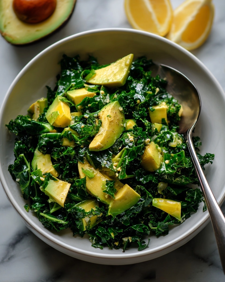 A white bowl filled with a green kale salad forms the base layer, showing curly and dark leafy kale pieces. On top, there are chunks of light green avocado unevenly spread over the kale. The salad is sprinkled with small black pepper flakes and tiny bits of lemon zest, giving texture and bright spots. A silver spoon rests inside the bowl on the right side, touching the salad. In the background, a halved avocado and a lemon wedge sit on a white marbled surface, adding a fresh, natural feel. Photo taken with an iphone --ar 4:5 --v 7