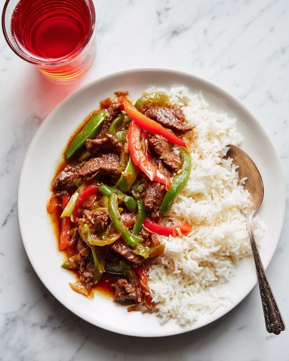 A white plate filled with two layers: the bottom layer is white rice with soft round grains, and the top layer has a mix of brown cooked meat strips coated in sauce, bright red and green strips of cooked bell peppers, all glistening with sauce. A silver spoon rests on the right side of the plate partially inside the food. The plate is placed on a white marbled surface, and a glass of dark reddish liquid is visible near the top left corner. photo taken with an iphone --ar 4:5 --v 7