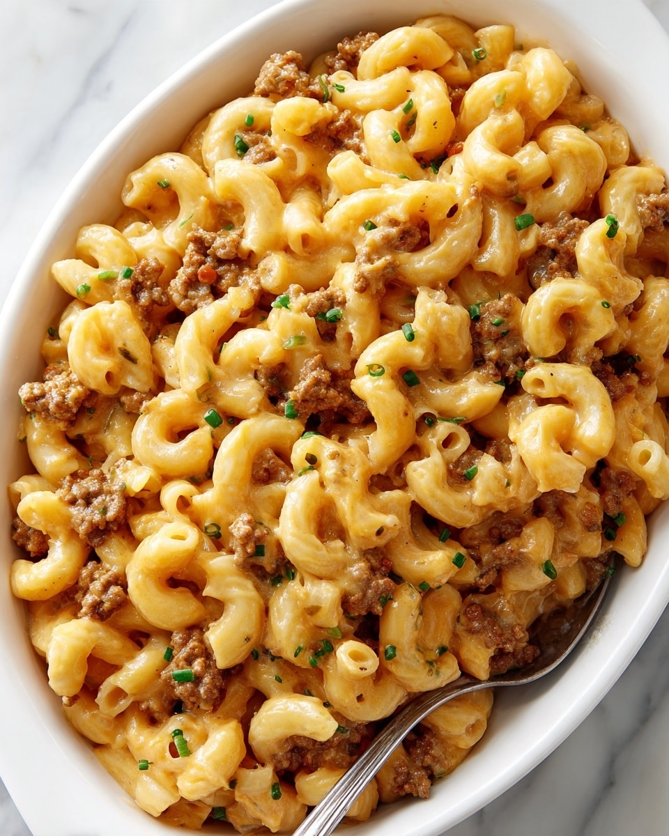 A close-up view of a white oval dish filled with creamy macaroni pasta mixed with browned ground meat and melted cheese sauce, all in shades of golden yellow and brown. The pasta pieces are curved tubes, evenly coated with the cheese sauce that gives a shiny, smooth texture. Small green herbs are scattered over the top, adding specks of color. A white spoon is partially dipped into the dish, lifting some pasta and sauce. The dish sits on a white marbled surface. photo taken with an iphone --ar 4:5 --v 7