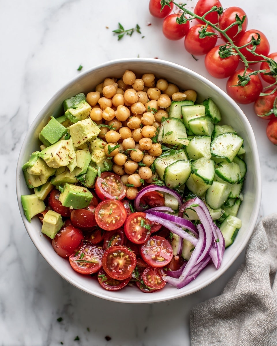 A close-up view of a black bowl filled with a colorful salad arranged in several layers: the base layer has light beige chickpeas scattered evenly, mixed with medium sized chunks of green avocado. On top of this are bright red tomato pieces, along with thin slices of purple onion, and small chopped pieces of dark green cucumber. The salad is lightly sprinkled with finely chopped herbs that add touches of green throughout. The bowl sits on a white marbled surface next to a beige cloth, and some red cherry tomatoes on the vine lie to the side. Photo taken with an iphone --ar 4:5 --v 7
