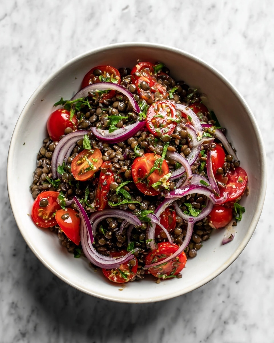 A white bowl filled with a lentil salad showing three main layers: the bottom layer is dark greenish-brown lentils, the middle layer has bright red cherry tomatoes, some whole and some sliced in half, and the top layer is thin rings of light purple and white onion mixed with small green herb pieces, all tossed together. The bowl is placed on a white marbled surface. photo taken with an iphone --ar 4:5 --v 7