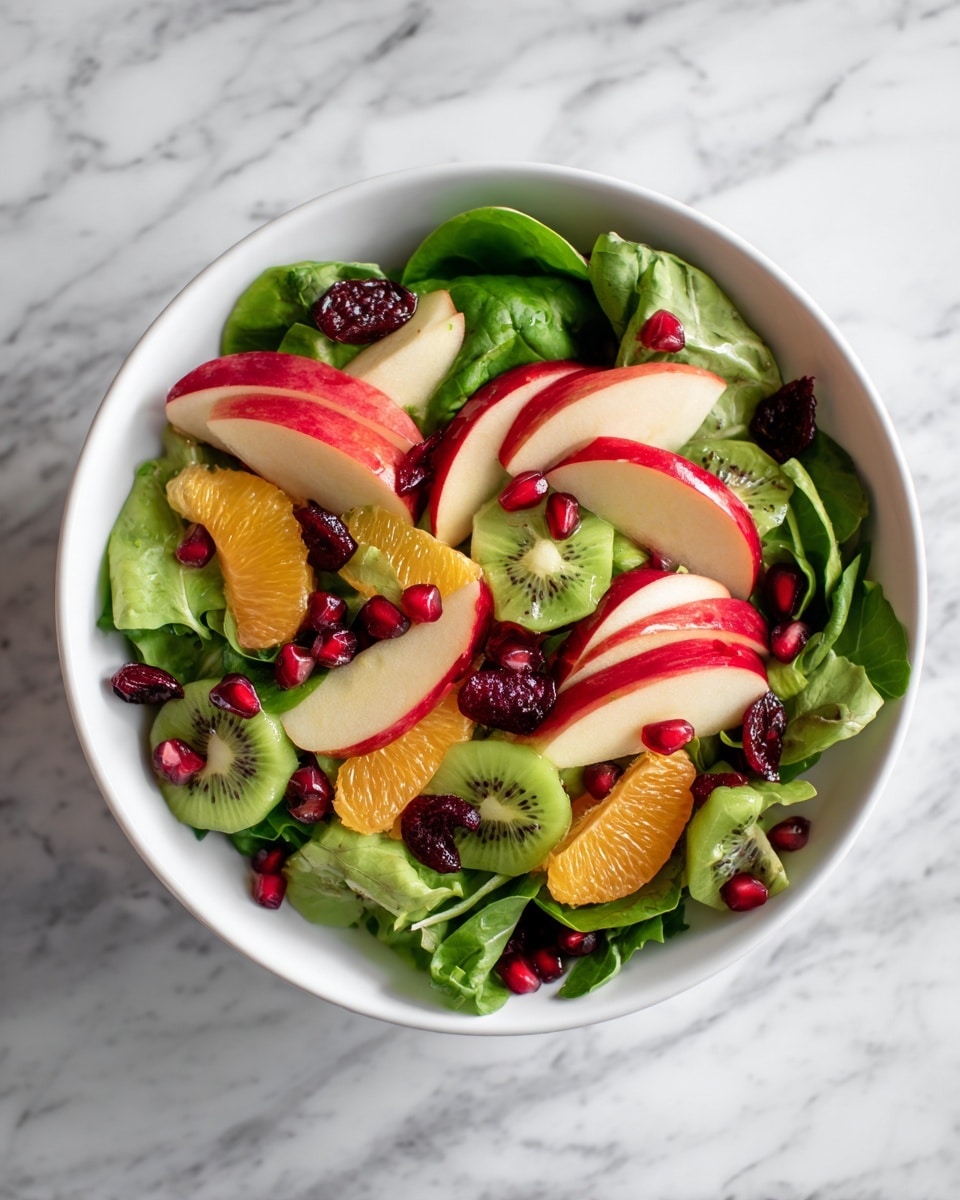 A white bowl filled with a colorful salad sits on a white marbled surface. The salad has one main layer made up of green leafy spinach, bright orange mandarin slices, diced red and pale green apples, translucent green kiwi slices, deep red dried cranberries, and shiny red pomegranate seeds scattered evenly on top. The colors mix well with various shades of green, orange, red, and white, creating a fresh and vibrant look. Photo taken with an iphone --ar 4:5 --v 7