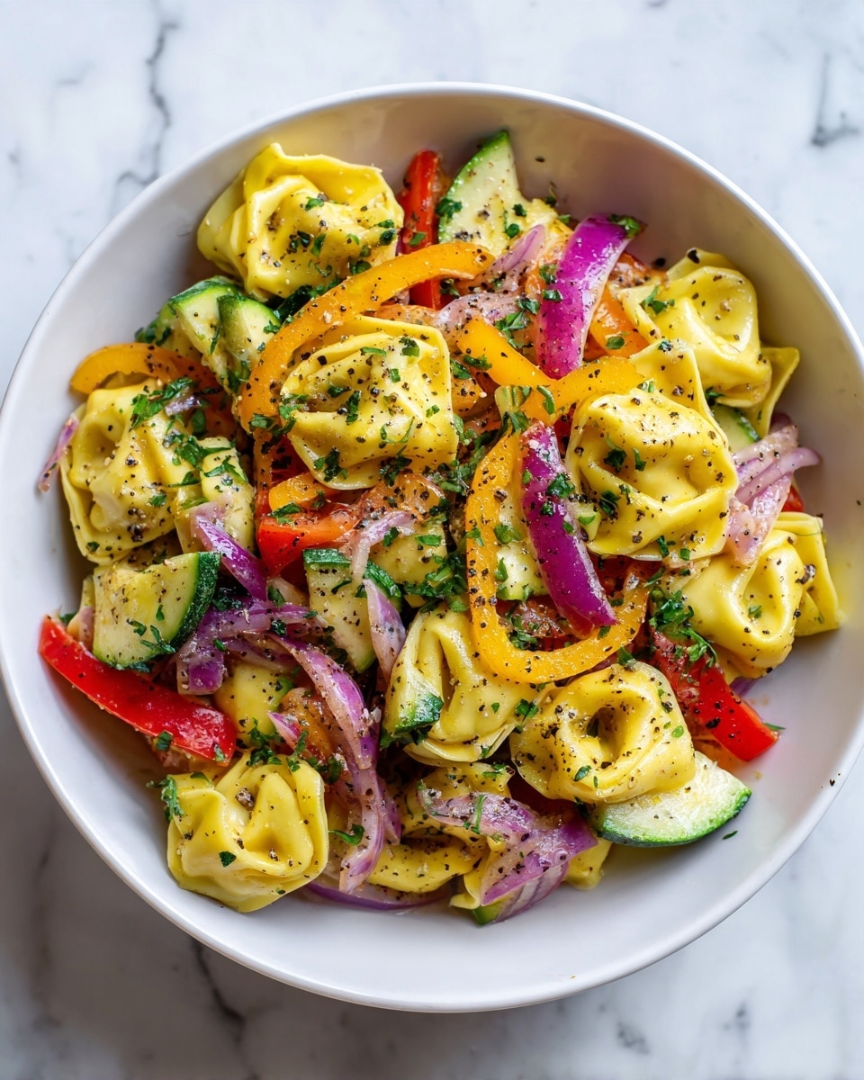A white bowl filled with a colorful tortellini pasta salad. The dish has three main layers: yellow tortellini pasta in the center with a soft, folded shape; thin slices of red and yellow bell peppers, and light green zucchini pieces scattered evenly among the pasta; thin strips of purple-red onion mixed throughout. The salad is sprinkled with chopped green herbs and cracked black pepper, adding texture and speckles of black and green all over. The bowl sits on a white marbled surface. photo taken with an iphone --ar 4:5 --v 7